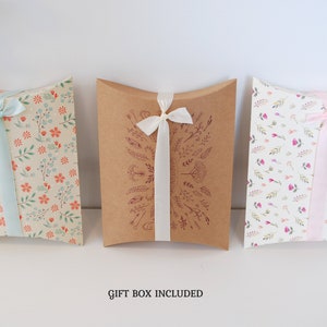 May include: Three pillow boxes with floral patterns and ribbon ties. The boxes are brown, cream, and white with different floral designs. The text "GIFT BOX INCLUDED" is printed below the boxes.