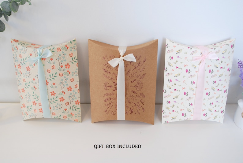 May include: Three pillow boxes with floral patterns and ribbon ties. The boxes are brown, cream, and white with different floral designs. The text "GIFT BOX INCLUDED" is printed below the boxes.