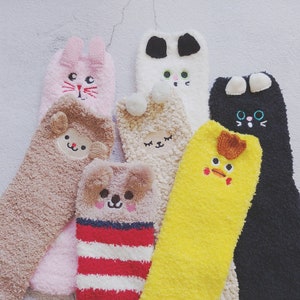 Könnte beinhalten: Sechs Paar flauschige Socken mit verschiedenen Tiergesichtern, die darauf gestickt sind. Die Socken sind in verschiedenen Farben, darunter rosa, braun, weiß, gelb und schwarz.