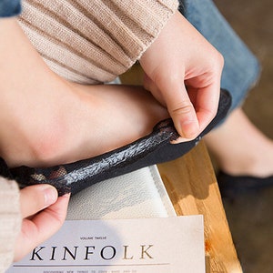 Może przedstawiać: Czarne skarpetki niewidoczne z delikatnym koronkowym wykończeniem. Skarpetki są trzymane przez osobę. Słowo "KINfolk" jest widoczne na magazynie. Zaprojektowane do noszenia z płaskimi butami.