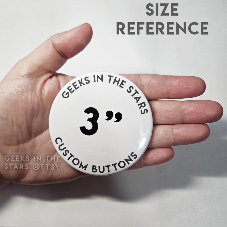 Peut inclure: Un bouton personnalis&eacute; blanc avec le texte "GEEKS IN THE STARS" et "CUSTOM BUTTONS" dans un design circulaire. Le bouton mesure 7,6 cm de diam&egrave;tre. Le texte "SIZE REFERENCE" est au-dessus du bouton.