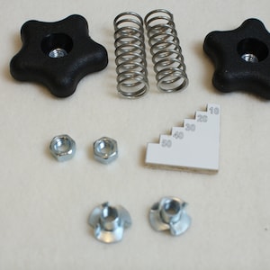 May include: A set of hardware parts for furniture assembly, including two black star-shaped knobs, two metal springs, two silver nuts, two silver wing nuts, and a white plastic ruler with markings from 10 to 50.