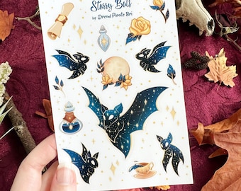 Może przedstawiać: Arkusz naklejek zatytułowany Starry Bats by Dread Pirate Bri z ilustracjami nietoperzy z ciemnoniebieskimi, gwiaździstymi skrzydłami, pełnią księżyca, żółtymi różami, buteleczkami z miksturami, zwojem i filiżanką herbaty.