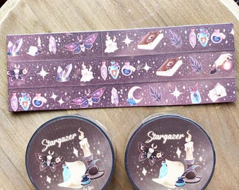 May include: Two circular rolls of washi tape and one rectangular strip of washi tape featuring a dark purple background with illustrations of moths, crystals, candles, books, potion bottles, and stars. The text Stargazer and Dread Pirate Bri is printed on the circular labels.