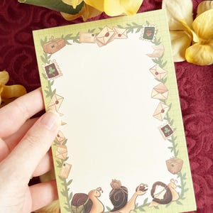 May include: A rectangular piece of stationery paper with a light green grid background. The border features a green vine pattern decorated with illustrations of envelopes, packages, postage stamps, and three snails at the bottom.