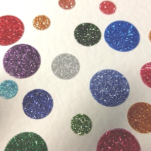 Könnte beinhalten: Eine Ansammlung glitzernder, farbenfroher Punkte in verschiedenen Größen. Die Punkte sind in den Farbtönen Grün, Rot, Lila, Blau, Gold und Silber auf einem weißen Hintergrund verteilt. Diese dekorativen Elemente könnten für Bastelarbeiten oder Verzierungen verwendet werden.