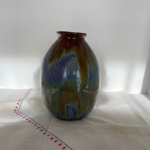 Peut inclure: Un vase en céramique avec un glaçage brun, vert et bleu. Le vase a une forme arrondie et une large ouverture.