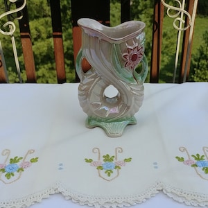 May include: A green and white ceramic vase with a floral design. The vase is shaped like a stylized flower with a hole in the center. The vase has a iridescent glaze.
