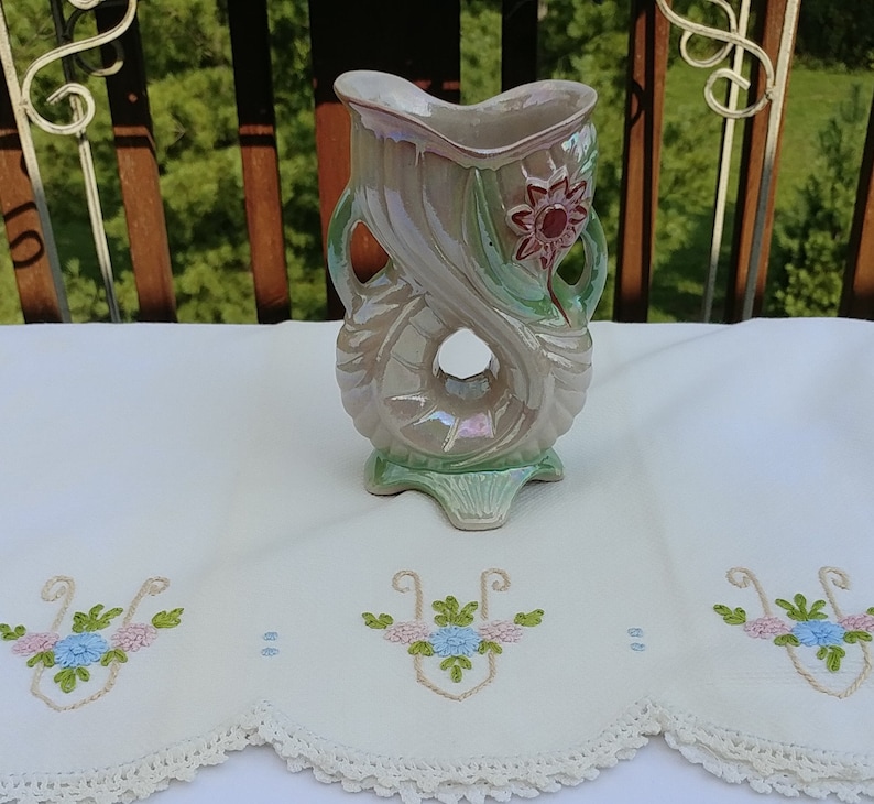 May include: A green and white ceramic vase with a floral design. The vase is shaped like a stylized flower with a hole in the center. The vase has a iridescent glaze.