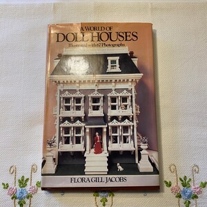 May include: A World of Doll Houses book with a photograph of a dollhouse on the cover. The dollhouse is white with black trim and has three stories. The book is by Flora Gill Jacobs and illustrated with 67 photographs.