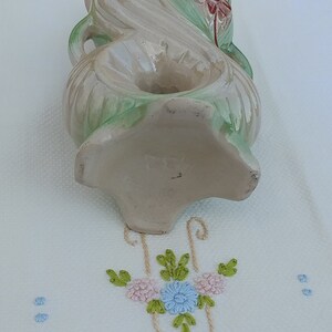 May include: A vintage ceramic vase with a floral design in shades of green, pink, and white. The vase has a unique shape with a double-loop handle and a floral motif on the bottom. The vase is marked with the number "282".