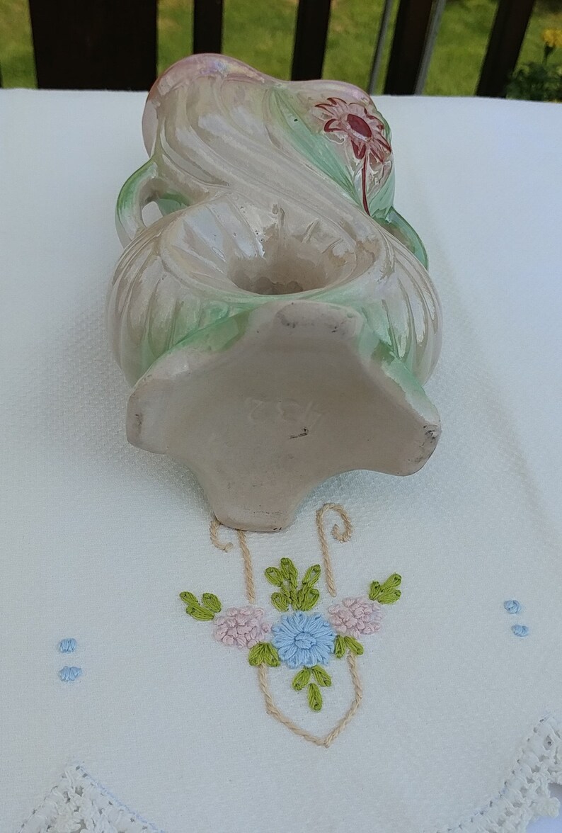 May include: A vintage ceramic vase with a floral design in shades of green, pink, and white. The vase has a unique shape with a double-loop handle and a floral motif on the bottom. The vase is marked with the number "282".