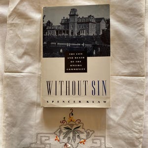 May include: A vintage hardcover book titled "Without Sin: The Life and Death of the Oneida Community" by Spencer Klaw. The cover features a black and white photograph of a large brick building.