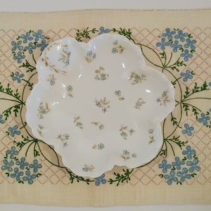 Könnte beinhalten: Eine weiße Porzellanservierschale mit gewelltem Rand und einem Blumenmuster. Die Schale ist mit kleinen blauen und grünen Blumen und goldenen Akzenten verziert.