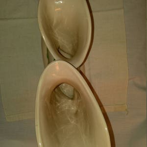 May include: A pair of vintage ceramic cream-colored vases with a green floral design. The vases are shaped like a trumpet or horn.