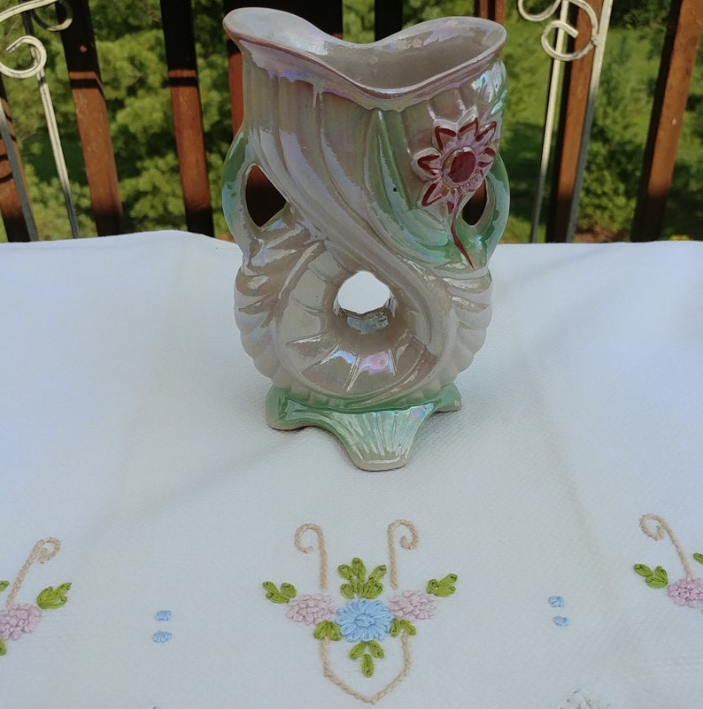 May include: A vintage iridescent ceramic vase with a floral design. The vase is shaped like a stylized flower with a hole in the center. The vase is green, pink, and white.