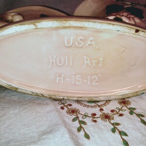 May include: A pink ceramic planter with a white oval label that reads "U.S.A. Hull Art H-15-12".