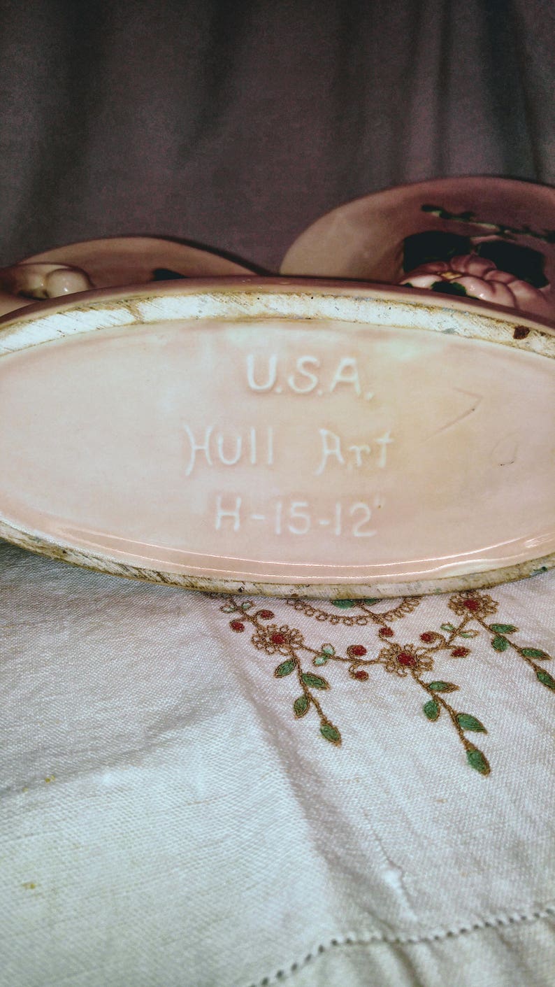 May include: A pink ceramic planter with a white oval label that reads "U.S.A. Hull Art H-15-12".