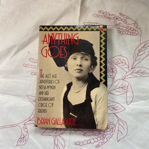 May include: A book titled "Anything Goes: The Jazz Age Adventures of Neysa McMein and Her Extravagant Circle of Friends" by Brian Gallagher. The cover features a black and white photograph of a woman wearing a black hat and a pearl necklace.