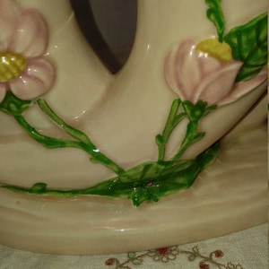 May include: A pair of ceramic vases with a pink and green floral design. The vases are shaped like a pair of intertwined swans with a delicate floral pattern.