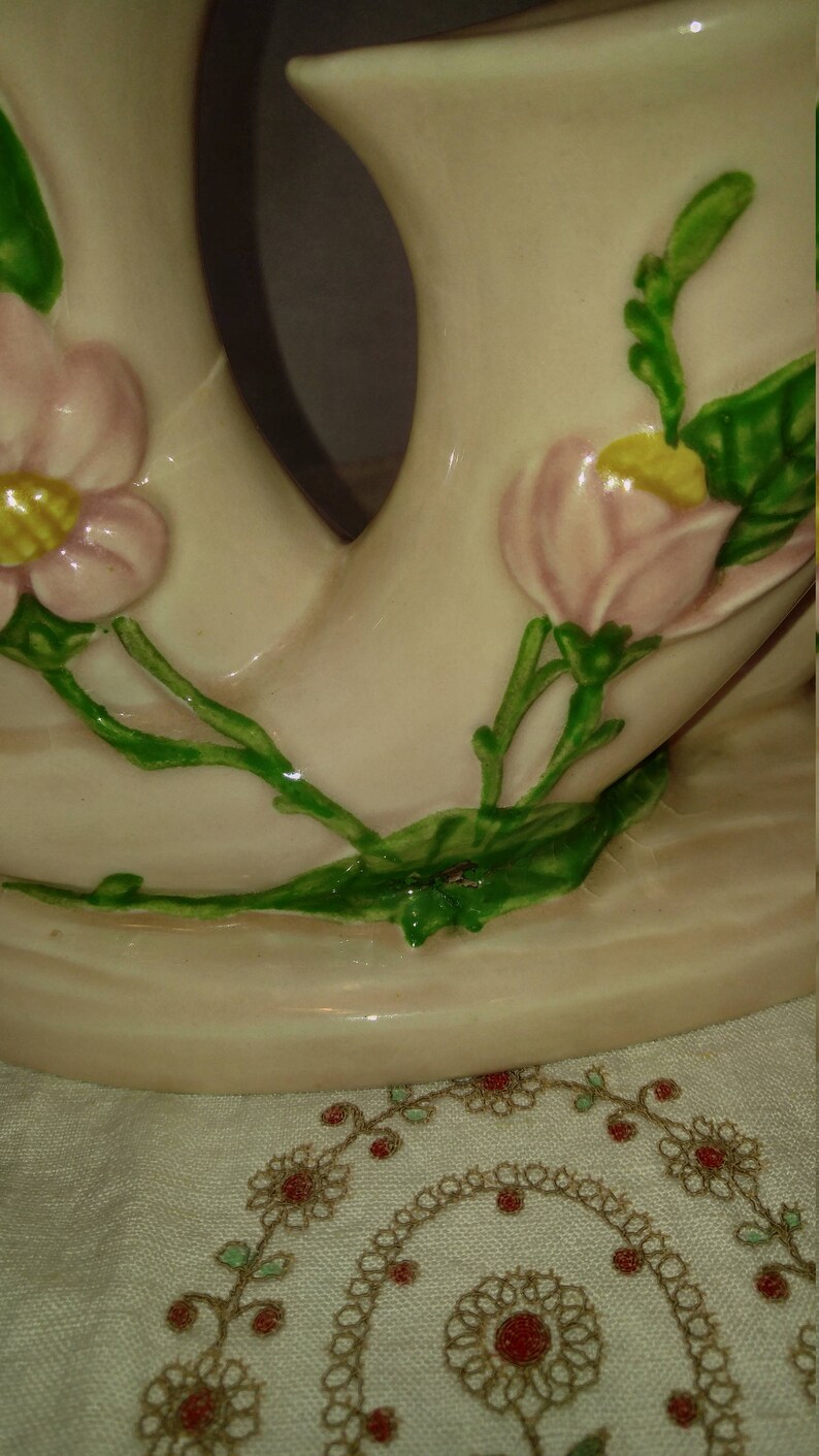 May include: A pair of ceramic vases with a pink and green floral design. The vases are shaped like a pair of intertwined swans with a delicate floral pattern.