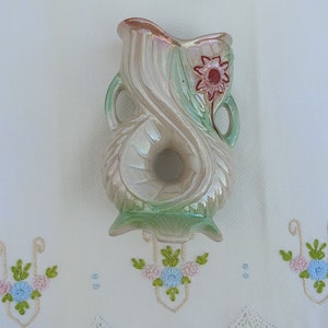 May include: A vintage ceramic vase with a pearlescent glaze and a green and white floral design. The vase has a unique shape with a hole in the center and a red flower with a yellow center.