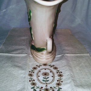 May include: A pink ceramic vase with green and pink floral designs. The vase has a wide opening and a narrow base.