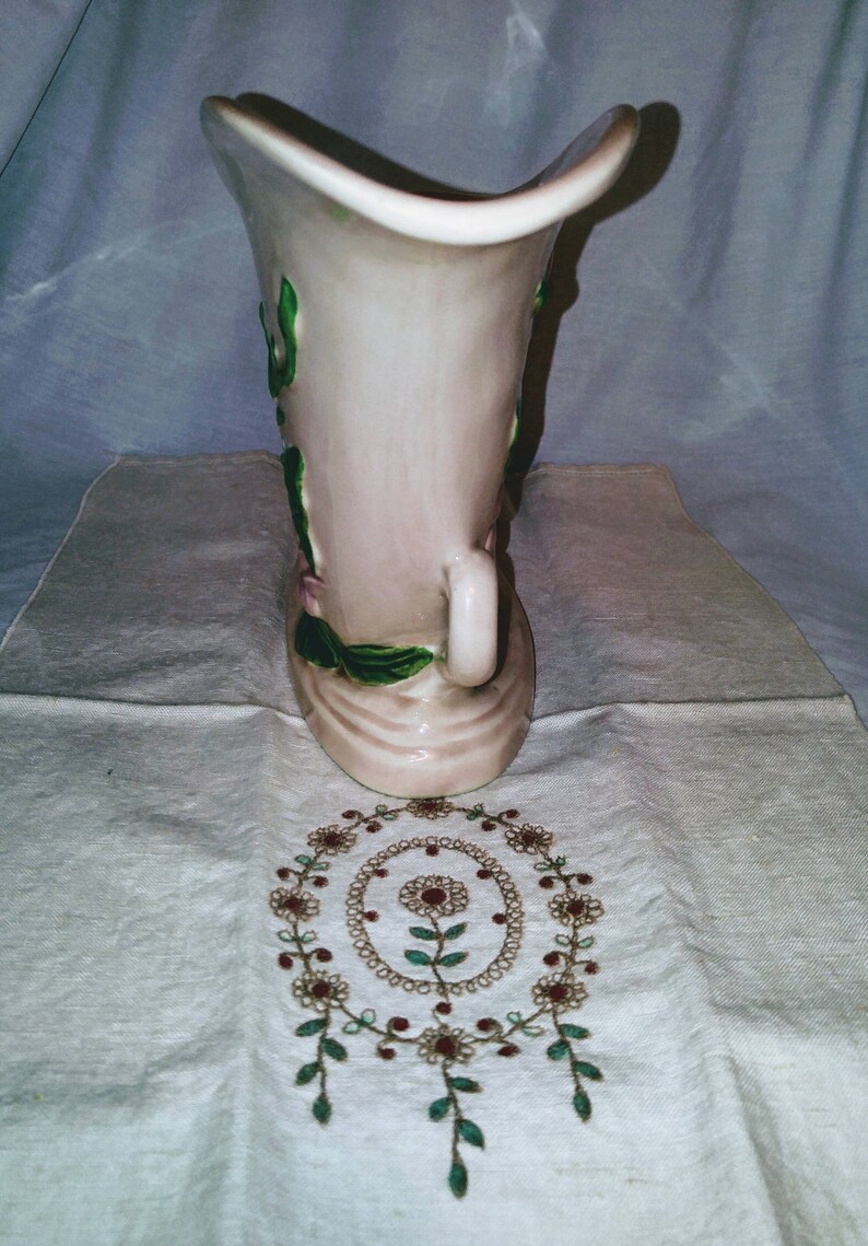 May include: A pink ceramic vase with green and pink floral designs. The vase has a wide opening and a narrow base.