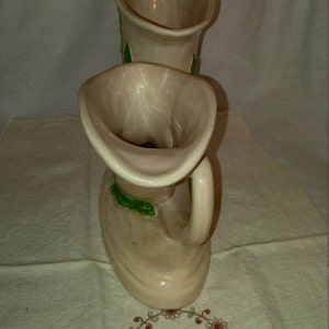 May include: Two ceramic vases shaped like a pair of boots with green leaf designs. The vases are a light beige color.
