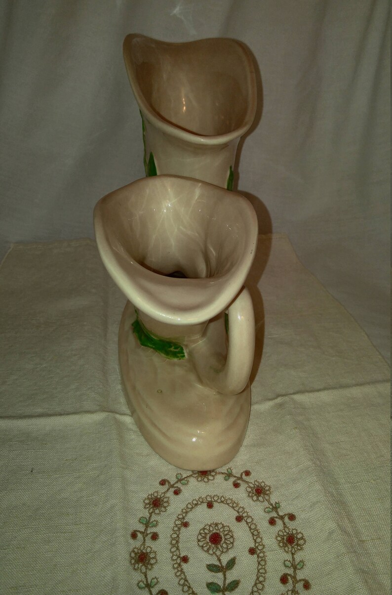 May include: Two ceramic vases shaped like a pair of boots with green leaf designs. The vases are a light beige color.