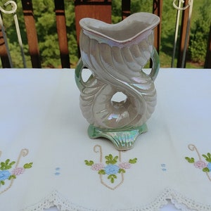 May include: A ceramic vase with a unique, swirling design. The vase is iridescent with a light gray and green color scheme.