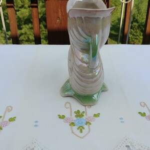 May include: A white ceramic vase with a green base and iridescent glaze. The vase is shaped like a stylized bird with a long neck and a curved body.