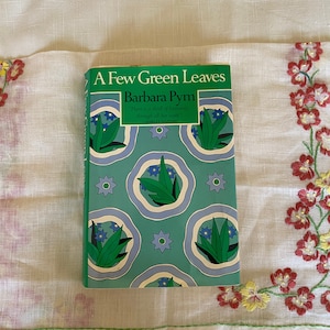 Puede incluir: Un libro de bolsillo titulado "A Few Green Leaves" de Barbara Pym. La portada presenta un fondo verde con un patrón repetido de círculos azules y blancos que contienen hojas verdes estilizadas y flores azules.