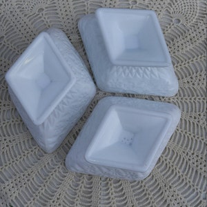 May include: Three white, diamond-shaped, milk glass dishes with a raised, textured design. The dishes are stacked on top of each other.