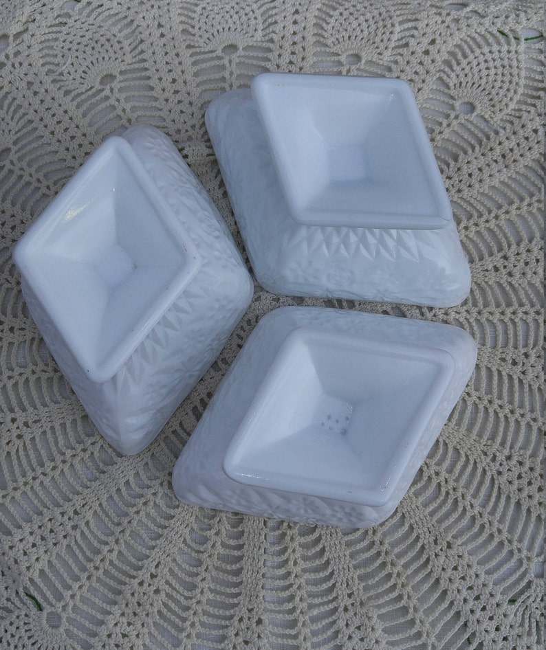 May include: Three white, diamond-shaped, milk glass dishes with a raised, textured design. The dishes are stacked on top of each other.