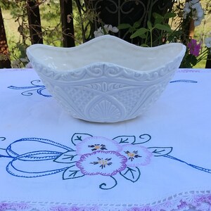 Pode incluir: Vaso de cerâmica branco com um design em relevo. O vaso tem uma borda festonada e tem a forma de um barco.