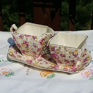 Könnte beinhalten: Ein Vintage-Sahne- und Zuckerset mit passendem Tablett. Das Set ist aus weißem Porzellan mit einem rosa, gelben und grünen Blumenmuster.