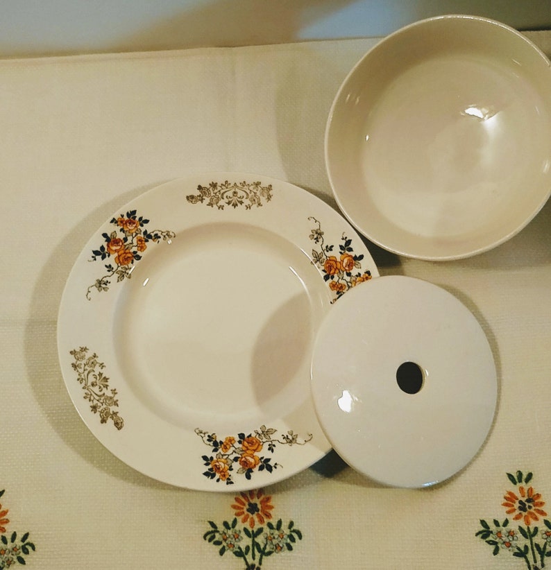 Puede incluir: Un juego de tres platos de cer&aacute;mica blanca con un dise&ntilde;o floral. Los platos tienen un borde elevado y un borde festoneado. El dise&ntilde;o floral presenta rosas amarillas y naranjas con hojas verdes.