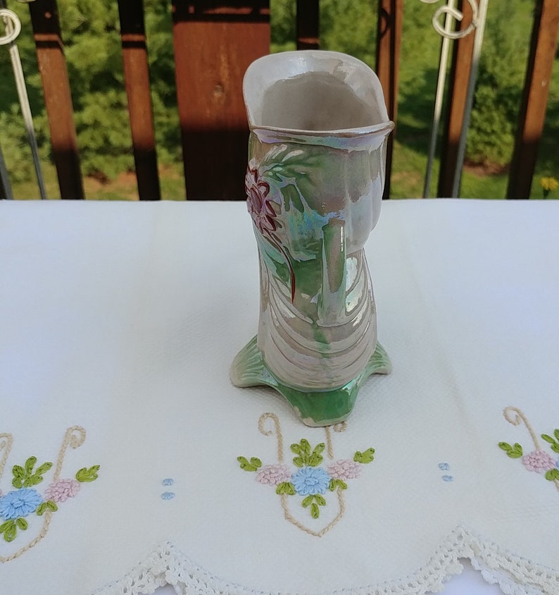 May include: A green and white ceramic vase with a floral design. The vase has a pearlescent glaze and is shaped like a boot.