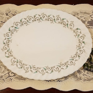 Peut inclure: Un plat de service ovale blanc avec un motif floral vert et or autour du bord.