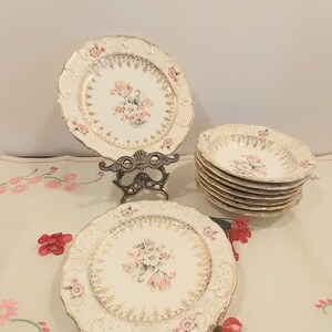 Può includere: Set di piatti vintage in porcellana bianca con bordo dorato e design floreale rosa. I piatti hanno un aspetto delicato e femminile e sarebbero perfetti per un tè o un'occasione speciale.