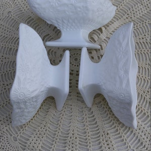 May include: Set of three white milk glass bud vases with a floral design. The vases are in the shape of a bowl with a wide base.
