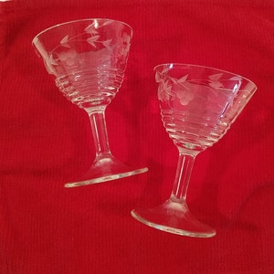 Op de afbeelding: Twee heldere glazen cocktailstelen met een gegraveerd bloemenmotief op een rode achtergrond.