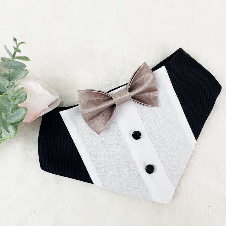 May include: A black and white dog bandana with a beige bow tie. The bandana has a tuxedo-style design with a white front and black sides.