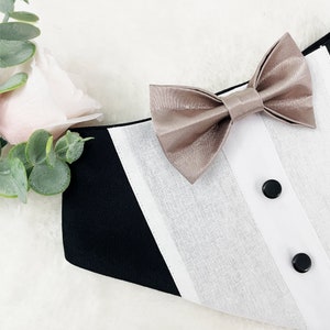 May include: A black and white tuxedo collar with a beige bow tie. The collar has two black buttons.