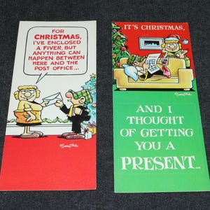 May include: Two Christmas greeting cards with cartoon illustrations. One card features a woman handing a letter to a man, with text: "For Christmas, I've enclosed a fiver, but anything can happen between here and the post office..." The other card has a person on a couch with text: "It's Christmas, and I thought of getting you a present..."