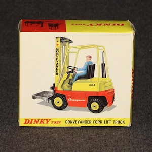 May include: A vintage Dinky Toys box featuring a yellow, red, and black Conveyancer Fork Lift Truck toy. The box has the text "Dinky Toys Conveyancer Fork Lift Truck" and an illustration of the toy.
