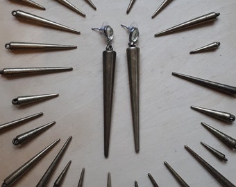 Può includere: Un paio di orecchini lunghi color bronzo con un design conico a punta. Gli orecchini sono esposti con diverse punte di bronzo più piccole e simili, creando un motivo radiale. Gli orecchini hanno una chiusura a perno con una gemma trasparente di forma ovale.