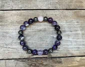 May include: A bracelet made of amethyst and hematite beads. The bracelet has a light pink bead in the center.