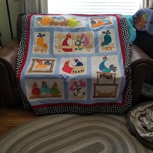 Pu&ograve; includere: Una trapunta fatta a mano con un design patchwork con applicazioni a tema gallina. La trapunta presenta uno sfondo blu e bianco, bordi rossi e un bordo a pois bianchi e neri. &Egrave; drappeggiata su una poltrona in pelle marrone.